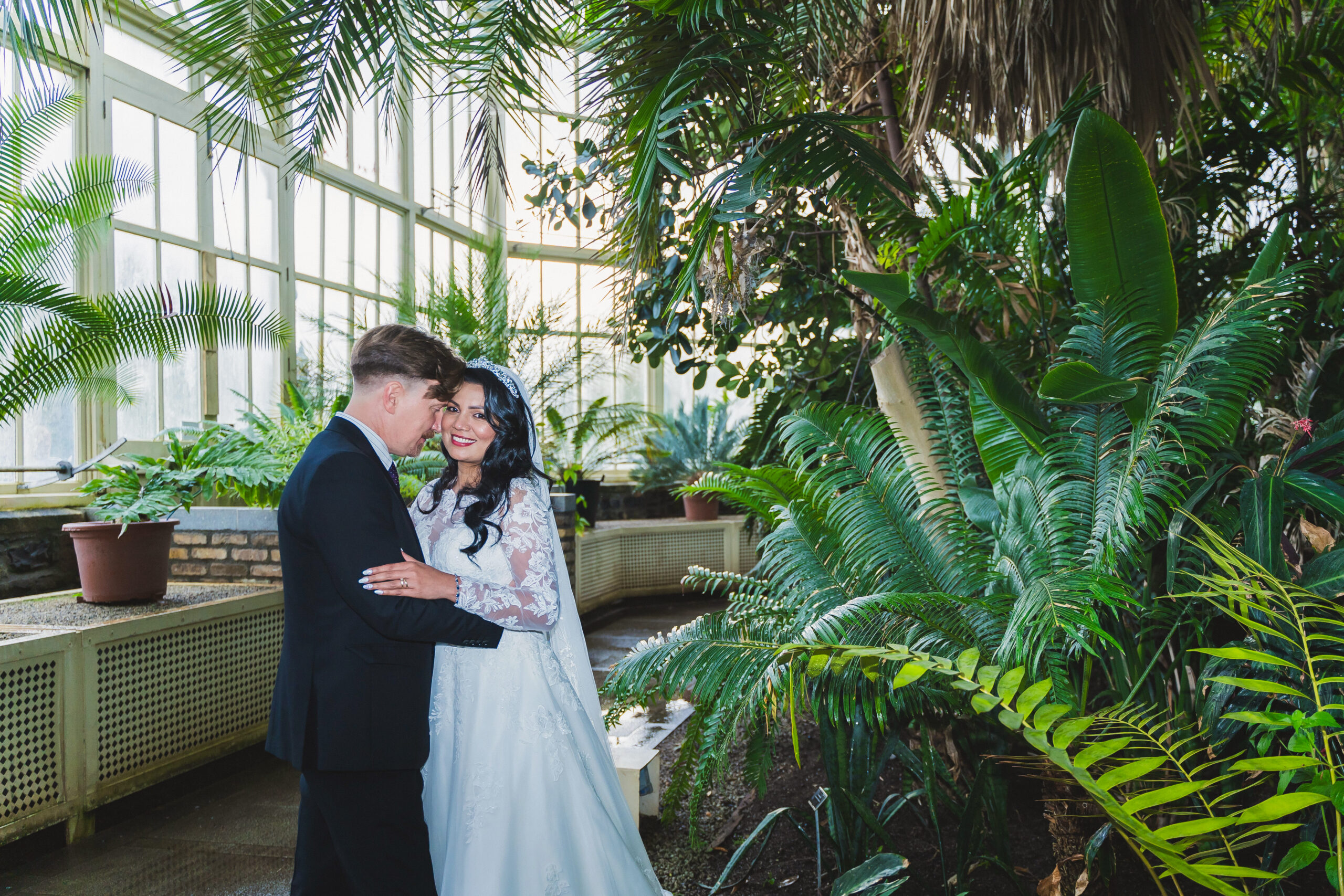 Couple in wedding attire embracing in a greenhouse